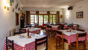 A restaurant with multiple tables covered in red and white checkered tablecloths, wooden chairs, and a tiled floor. - Hostal Casa Manolo (La Senia)