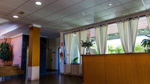 A reception area with a wooden counter, a potted plant, and a view of the outdoors through a window with curtains. - Hostal Casa Manolo (La Senia)