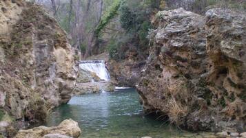 A natural landscape with a waterfall, rocky terrain, and a clear stream.