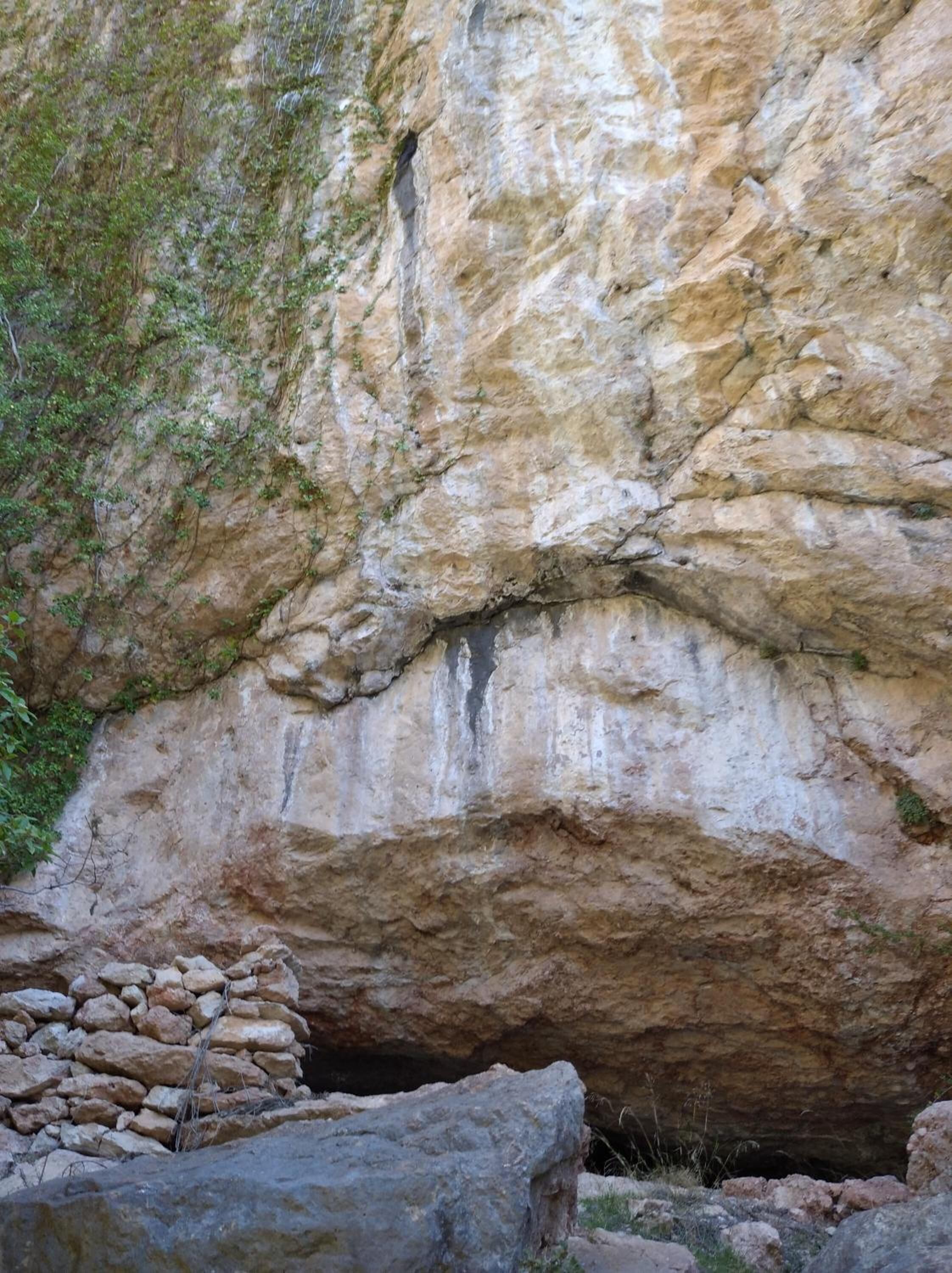 A natural rock formation with a cave entrance and a stone structure nearby.