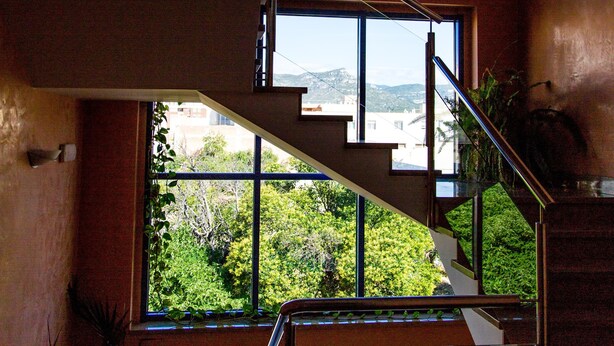 A modern interior with a staircase leading to an upper level, large windows offering a view of greenery outside. - Hostal Casa Manolo (La Senia)