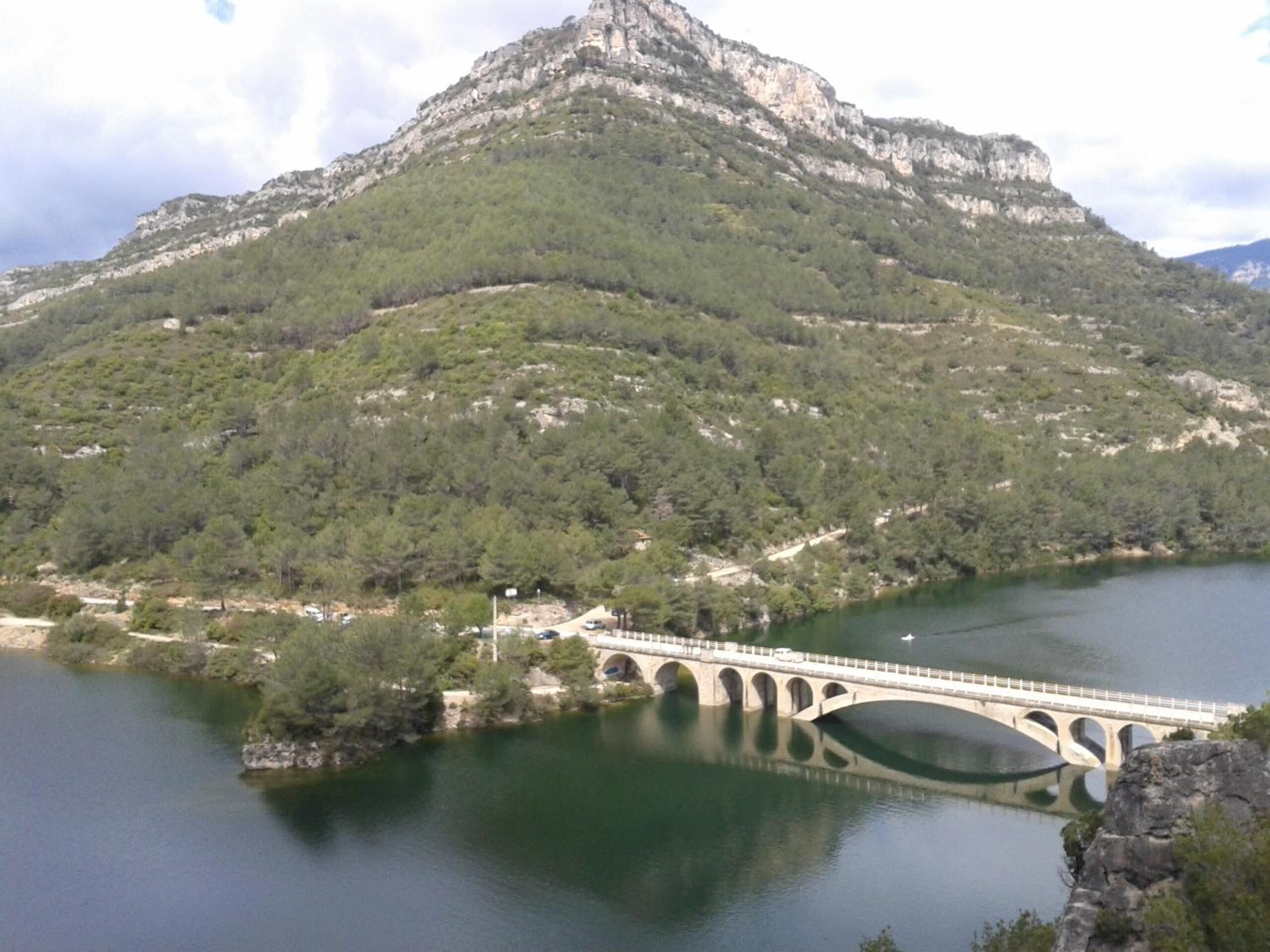 A stone bridge over a calm lake with a mountainous backdrop.