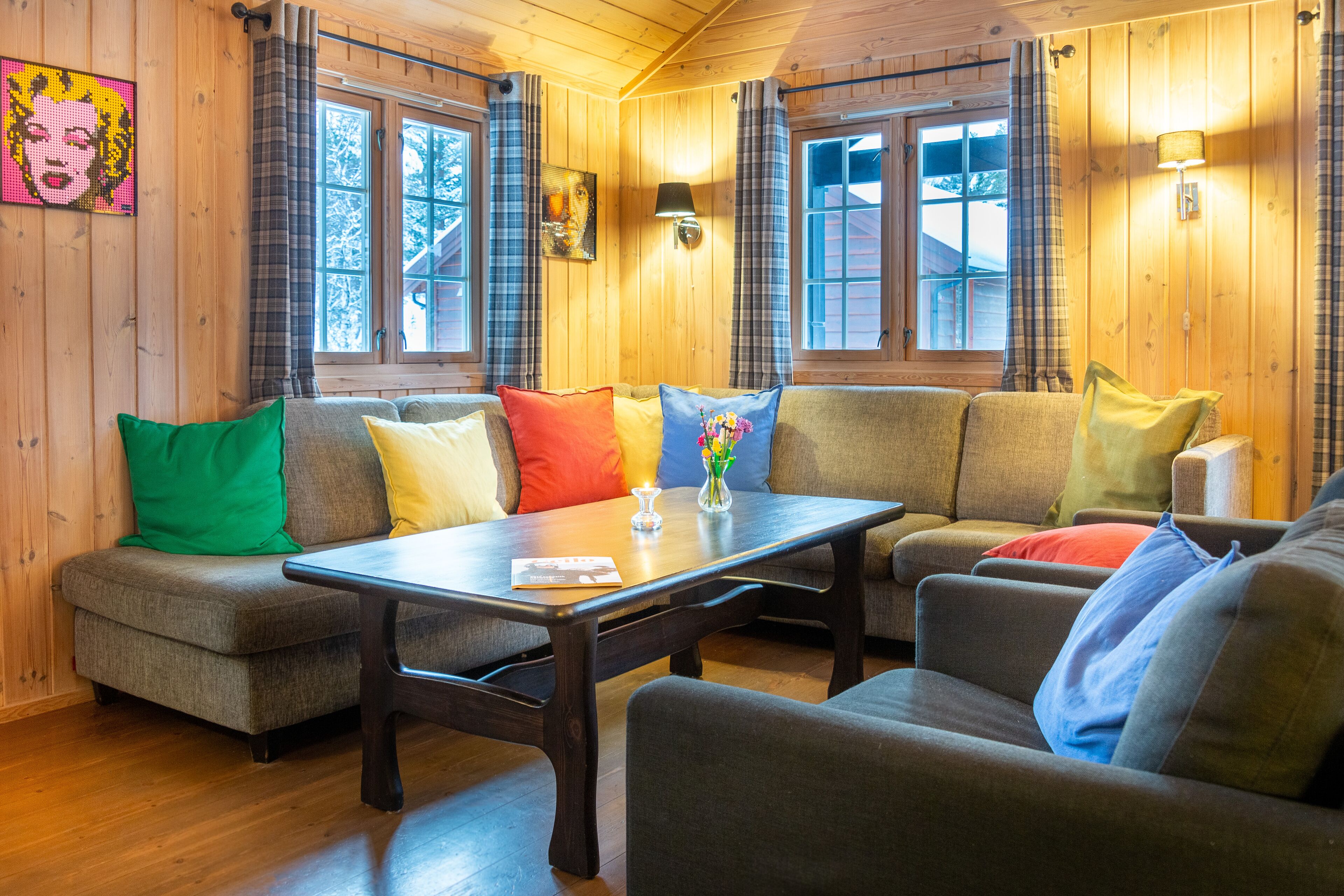 L’intérieur d’un chalet chaleureux, avec un ensemble de canapés, une table en bois et des rideaux à carreaux.