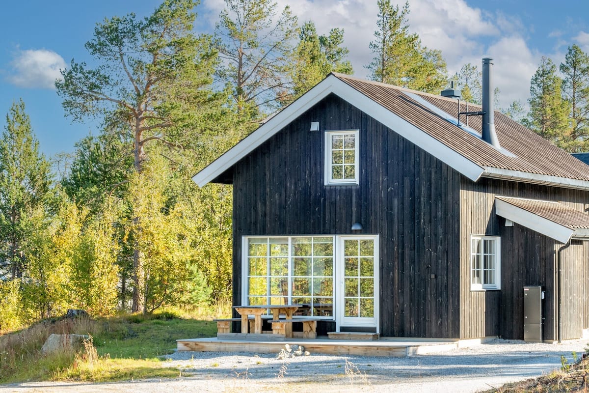 A wooden cabin with a large window, a chimney, and a small porch.