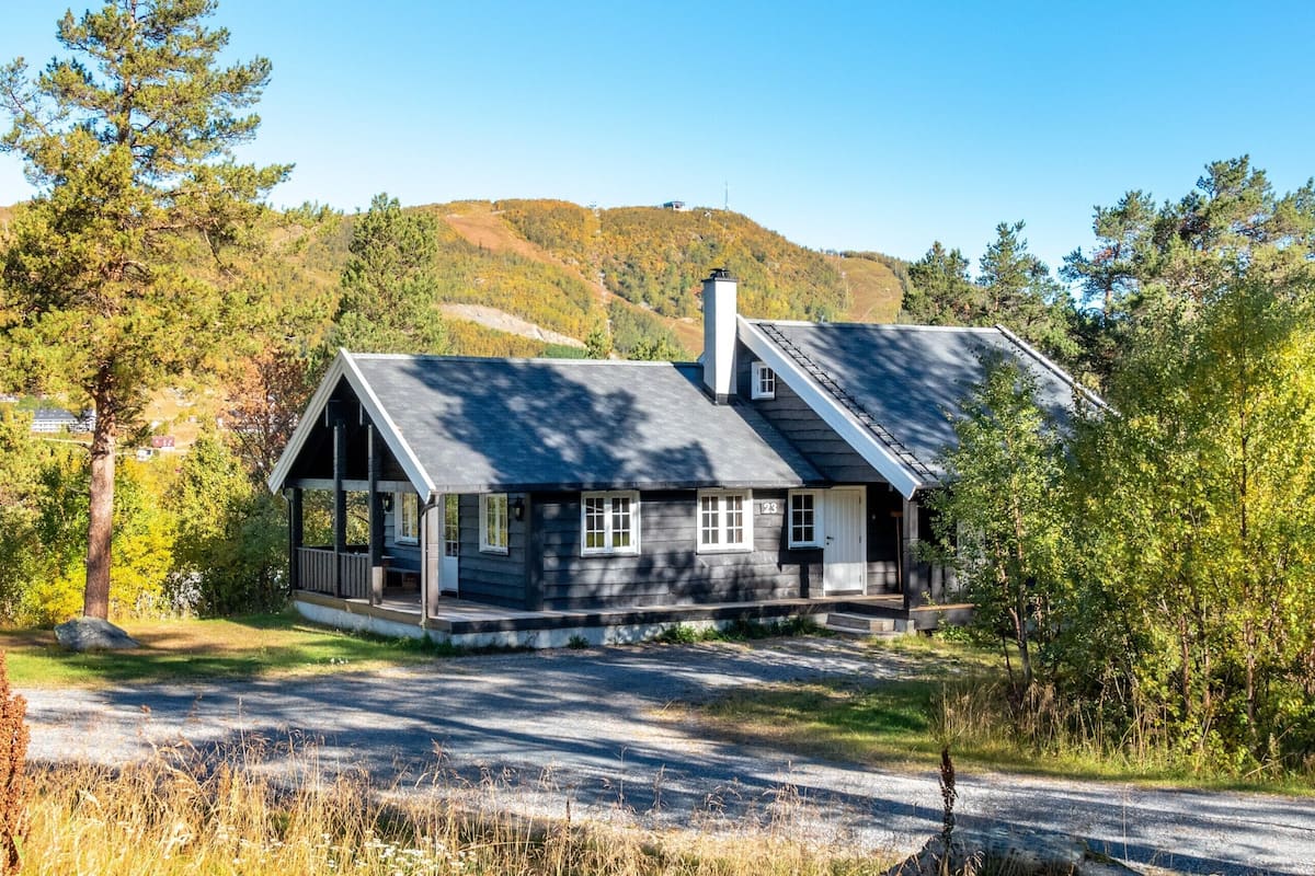 A two-story house with a porch, surrounded by trees and hills.