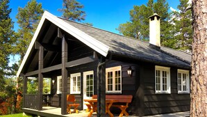 Une cabane dotée d’une véranda, de bancs en bois et d’une cheminée.