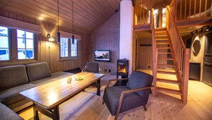 L’intérieur chaleureux d’un chalet, avec un revêtement mural en bois, une cheminée, un canapé, une table et un escalier.