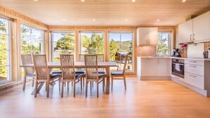 Une cuisine spacieuse avec des meubles en bois, un coin repas comprenant une table et des chaises, et de grandes fenêtres offrant une vue sur l’extérieur.