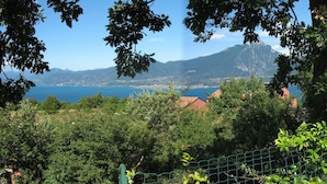 A house with a patio, surrounded by lush greenery and a view of a mountain and lake. - Villa Bardino (Torri del Benaco)