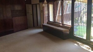 Une pièce avec un tapis beige, un canapé, une armoire et une fenêtre donnant sur un jardin.