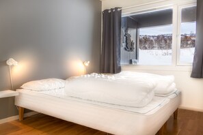A bedroom with a bed, bedside lamps, a window with curtains, and a view of a snowy landscape.