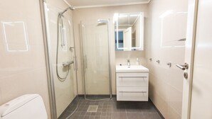 Un baño con ducha envuelta en vidrio, un lavabo blanco con espejo y un inodoro.