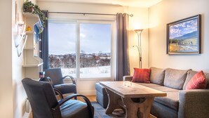 Una sala de estar moderna con un sofá, sillones, una mesa de centro de madera y un ventanal con vistas a un paisaje nevado.