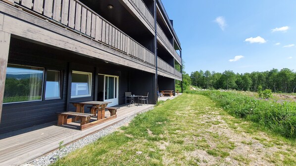 A modern building with a wooden deck, outdoor seating, and a view of the surrounding forest.
