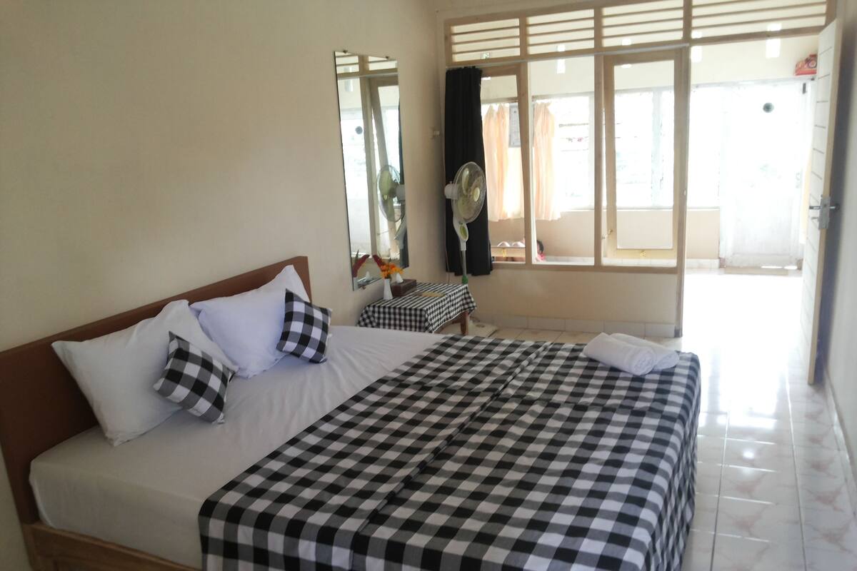 A hotel room with a large bed, a bedside table, a mirror, and a window with curtains.