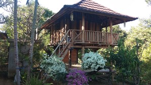 Une structure en bois dotée d’un balcon, entourée d’une végétation luxuriante et de plantes en fleurs.