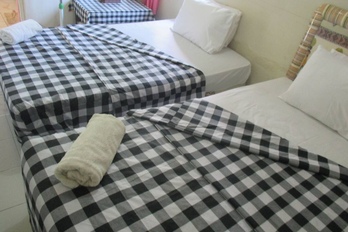 A hotel room with two beds, each with a checkered bedspread and white pillows.
