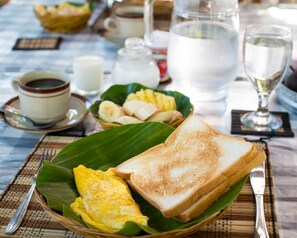 A breakfast setting with toast, eggs, and fruit on a banana leaf, along with cups of coffee and milk. - ESA di Kubu Homestay (Sawan)