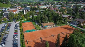 An aerial view of a town with a tennis court, surrounded by residential buildings and greenery.