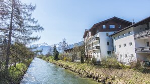A river running alongside a building with balconies and a mountain in the background.