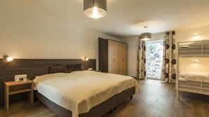 A bedroom with a large bed, wooden headboard, bedside table with a lamp, wardrobe, and a bunk bed in the corner.