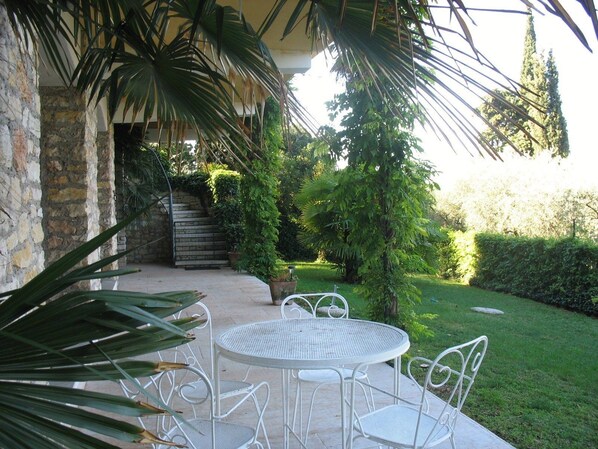 An outdoor patio with a round table and chairs, surrounded by greenery and a stone wall.