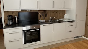 A modern kitchen with white cabinets, a black stove, and a stainless steel sink. - Slåttastølen Leiligheter by Geilolia (Hol)