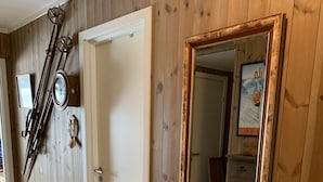 A room with wooden walls, a door, a mirror with a decorative frame, a bench, and skis leaning against the wall. - Slåttastølen Leiligheter by Geilolia (Hol)