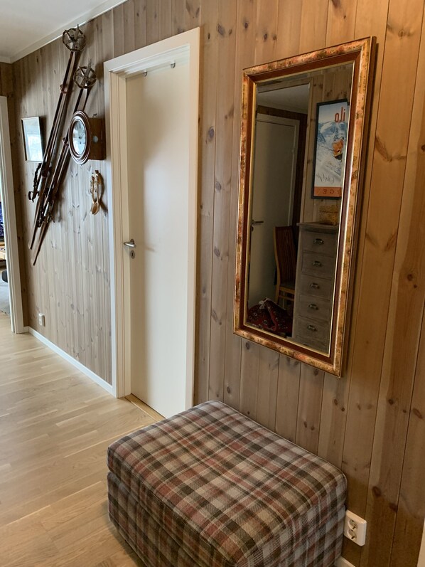A room with wooden walls, a door, a mirror with a decorative frame, a bench, and skis leaning against the wall. - Slåttastølen Leiligheter by Geilolia (Hol)
