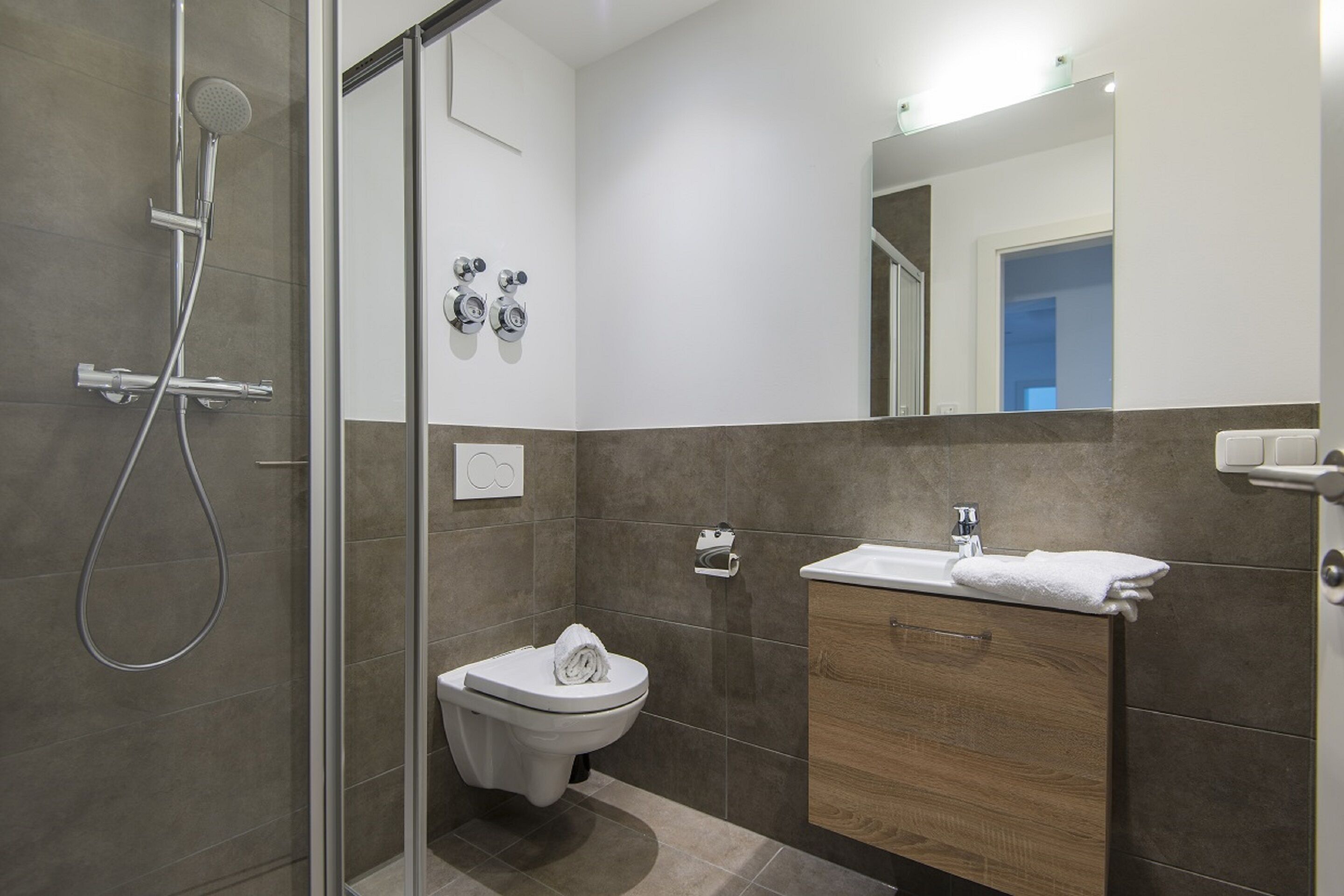 Une salle de bain moderne avec une douche à parois de verre, des toilettes et un meuble-lavabo avec un miroir.