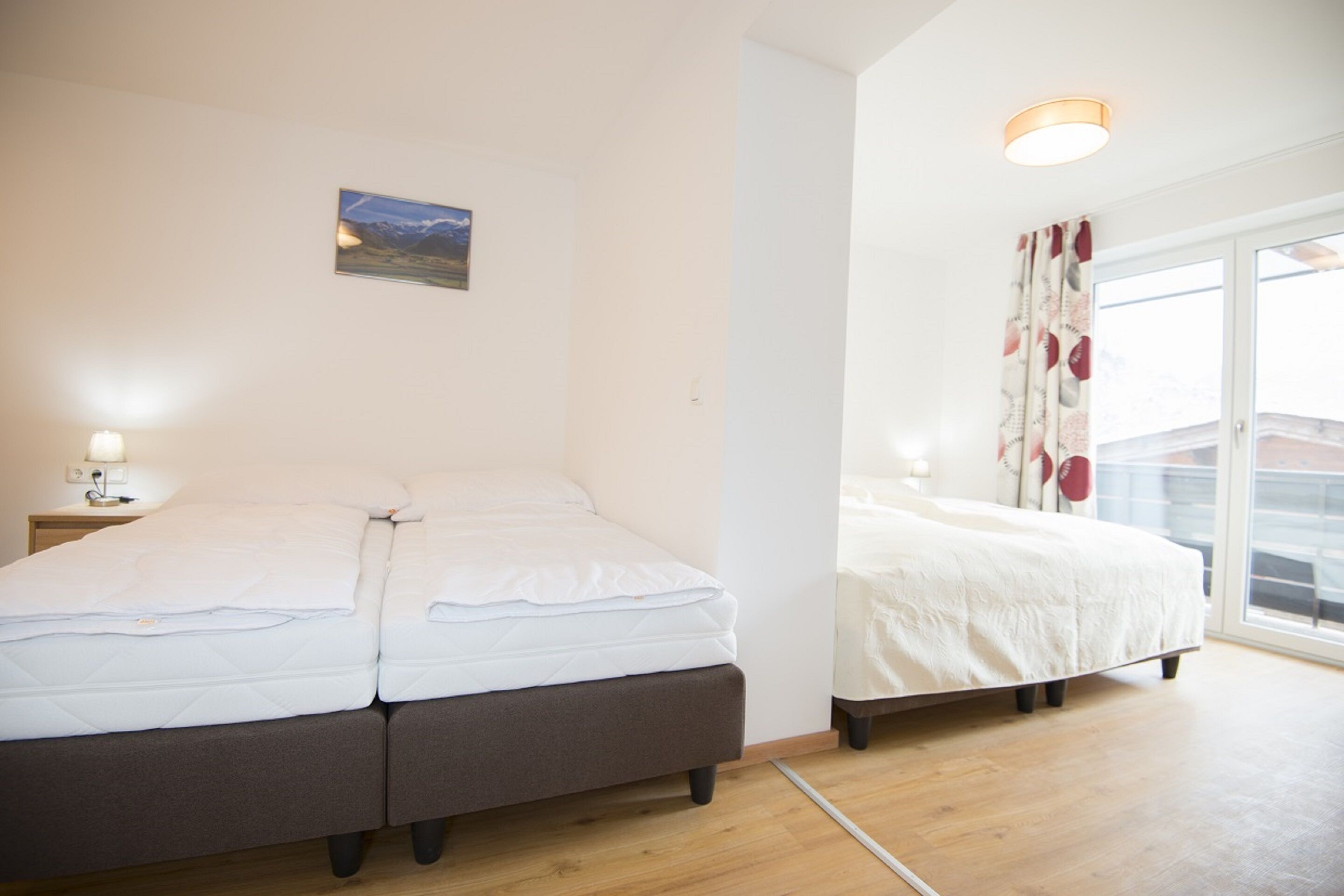 Un dormitorio con cama, mesita de noche, un cuadro en la pared y ventana con cortinas.