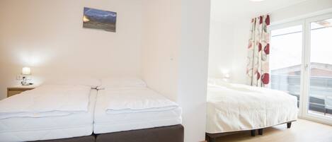 Un dormitorio con cama, mesita de noche, un cuadro en la pared y ventana con cortinas.