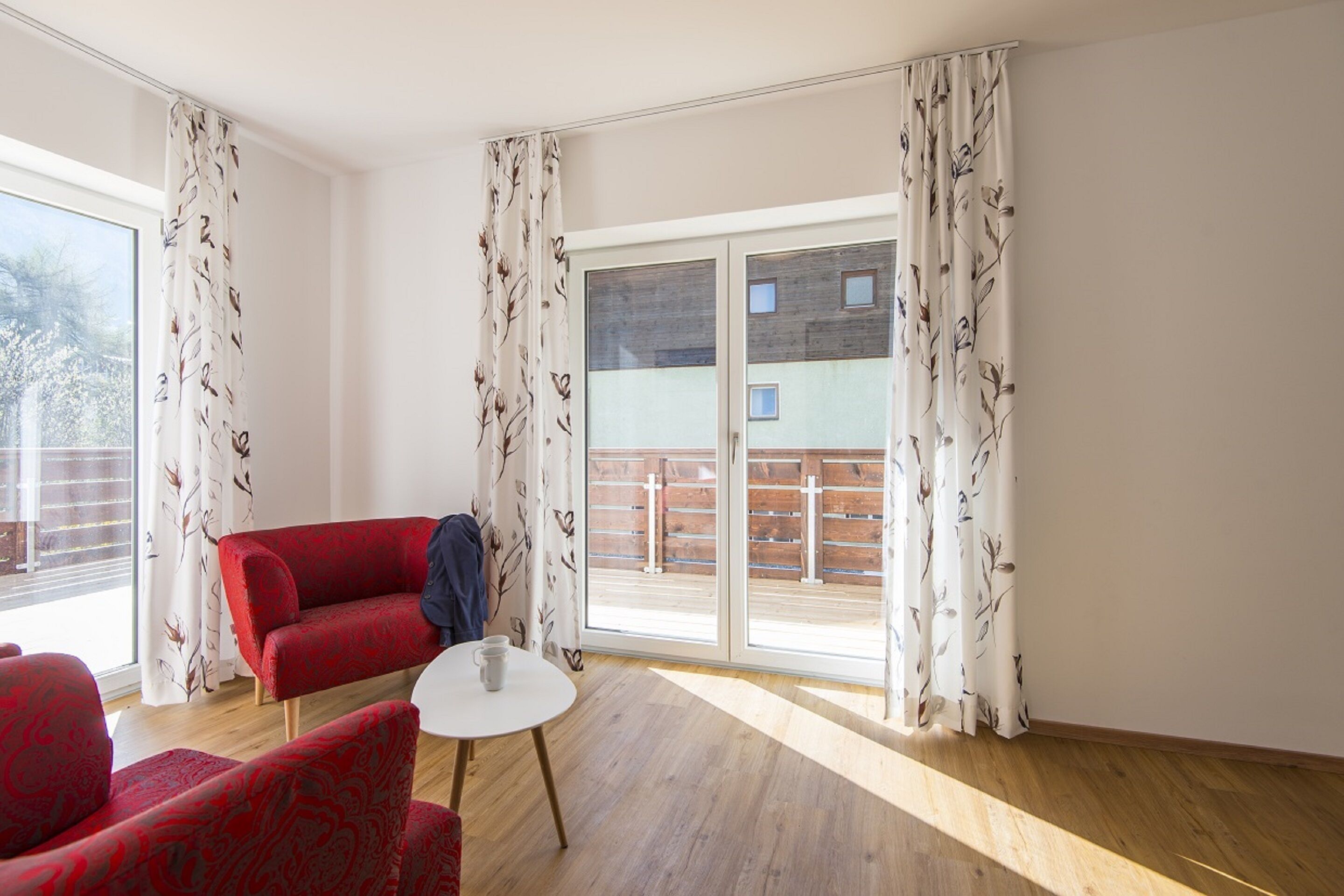 A room with a red sofa, a small round table, and a sliding glass door leading to an outdoor area.