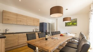 Une cuisine moderne avec des meubles en bois, une table à manger avec des chaises et des luminaires suspendus.
