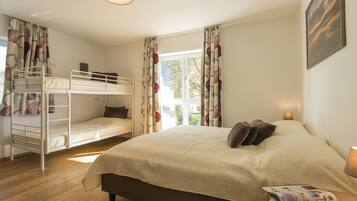 Une chambre avec un grand lit, un lit superposé, une fenêtre avec des rideaux, une lampe et un tableau encadré au mur.