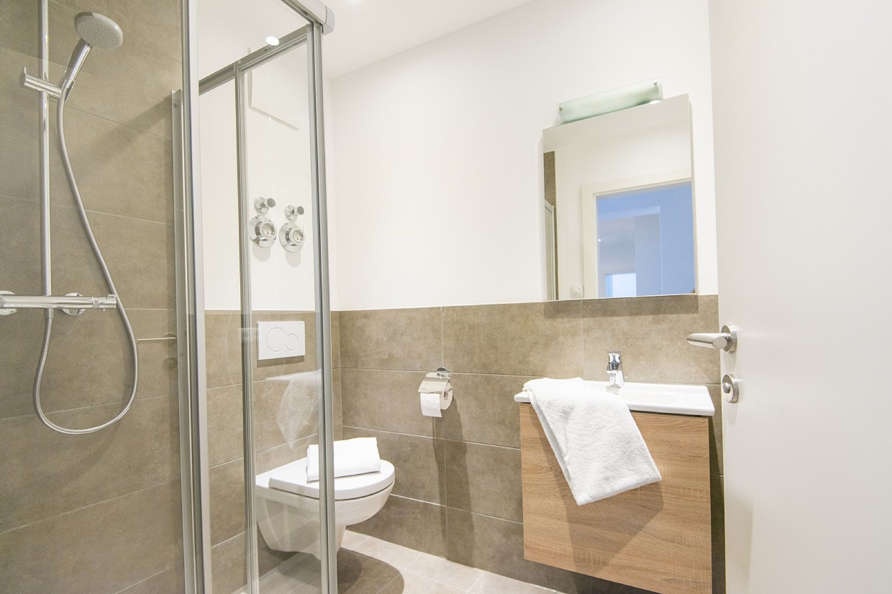 Un bagno moderno con box doccia in vetro, un water e un lavandino con un asciugamano appeso al muro.