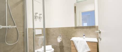 Un bagno moderno con box doccia in vetro, un water e un lavandino con un asciugamano appeso al muro.