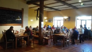 Un restaurante con mesas y sillas de madera, un menú en pizarra y amplios ventanales que dejan entrar luz natural.