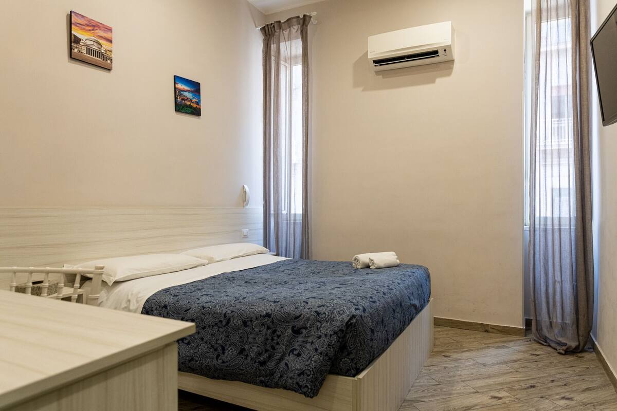 Un dormitorio con cama, una mesita de noche, un equipo de aire acondicionado y dos cuadros en la pared.