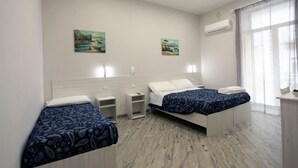 A bedroom with two beds, a nightstand, a small table, and a window with curtains. - B&B alla Ferrovia (Naples)