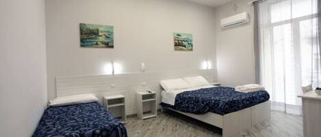A bedroom with two beds, a nightstand, a small table, and a window with curtains.