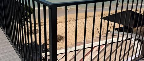 Una terraza de madera con barandilla metálica que da a una playa.