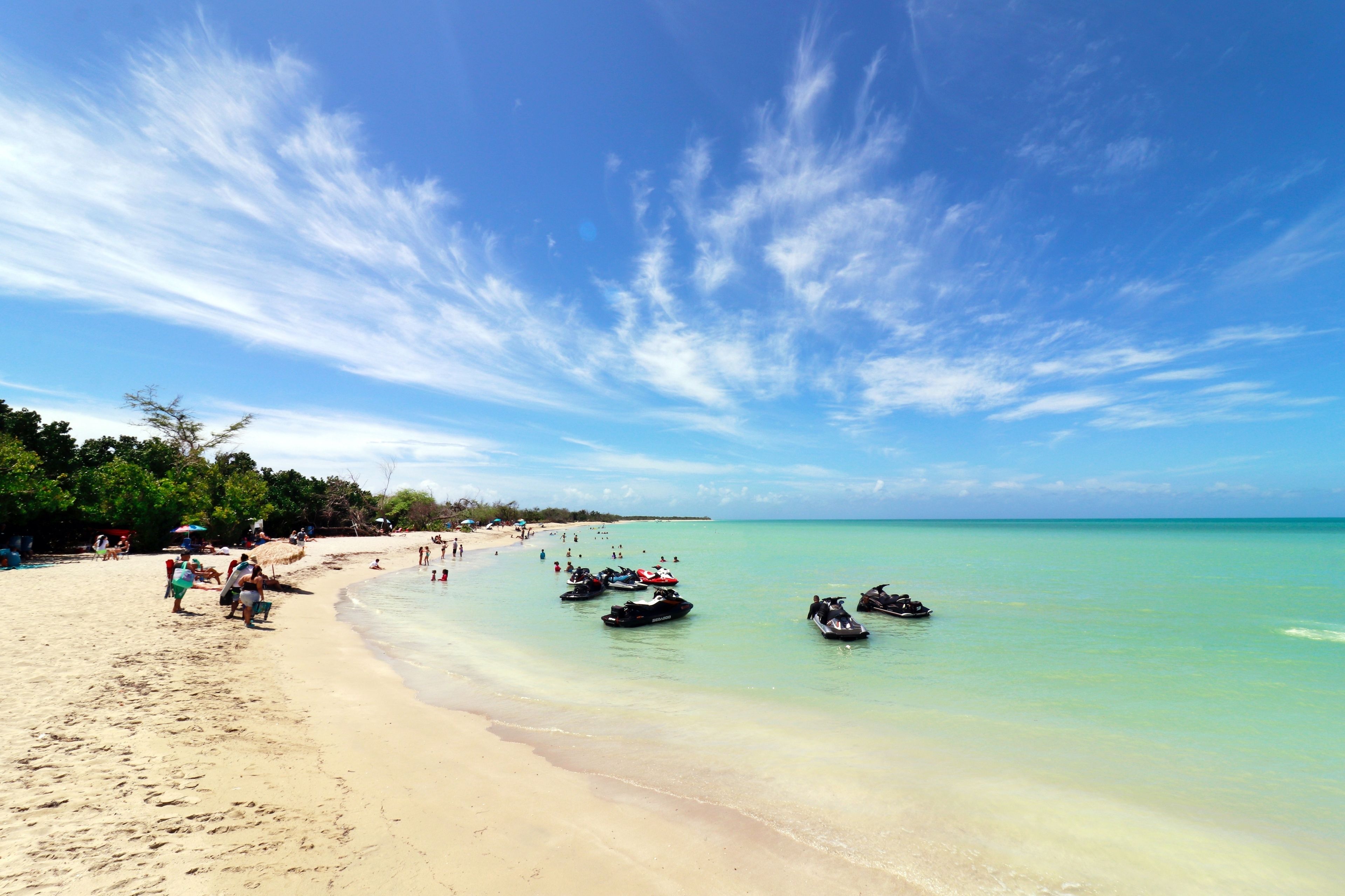 A beach with clear turquoise water, a sandy shore, and several jet skis.