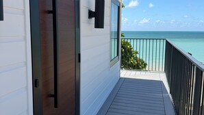 A wooden deck with a sliding door, a black wall-mounted light, and a view of the ocean. - Rooms Boutique by Annie's (Cabo Rojo)