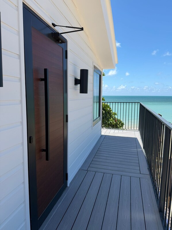 Um deck de madeira com porta de correr, uma luz preta fixada na parede e vista para o oceano.