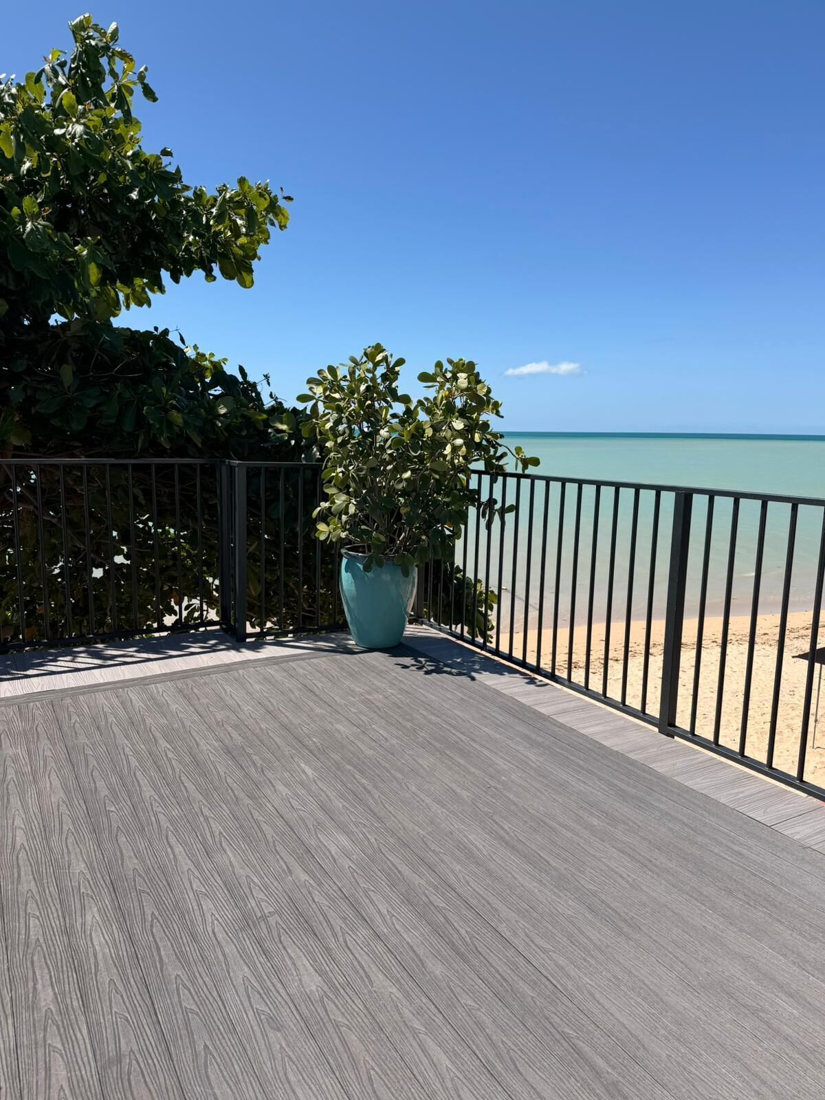 Eine Holzterrasse mit Metallgeländer, das auf einen Strand blickt.