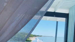 A balcony with a mesh screen, a glass table, and chairs, overlooking a beach and ocean. - Rooms Boutique by Annie's (Cabo Rojo)
