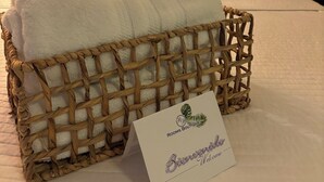 A neatly made bed with white linens, a woven basket with a white towel, and a welcome card on the side. - Rooms Boutique by Annie's (Cabo Rojo)
