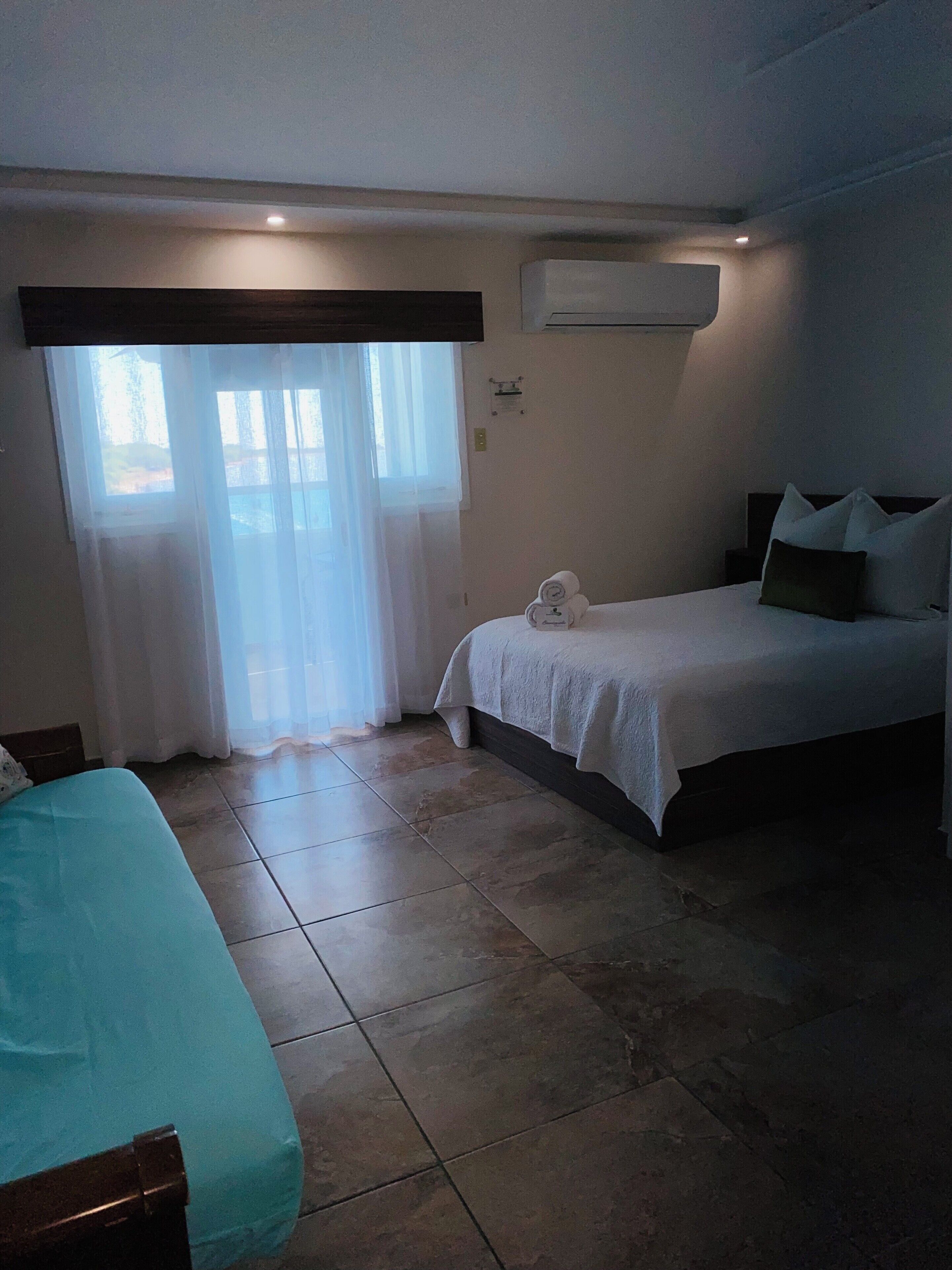 Una camera da letto con un letto, un comodino, una finestra con tende e un condizionatore.