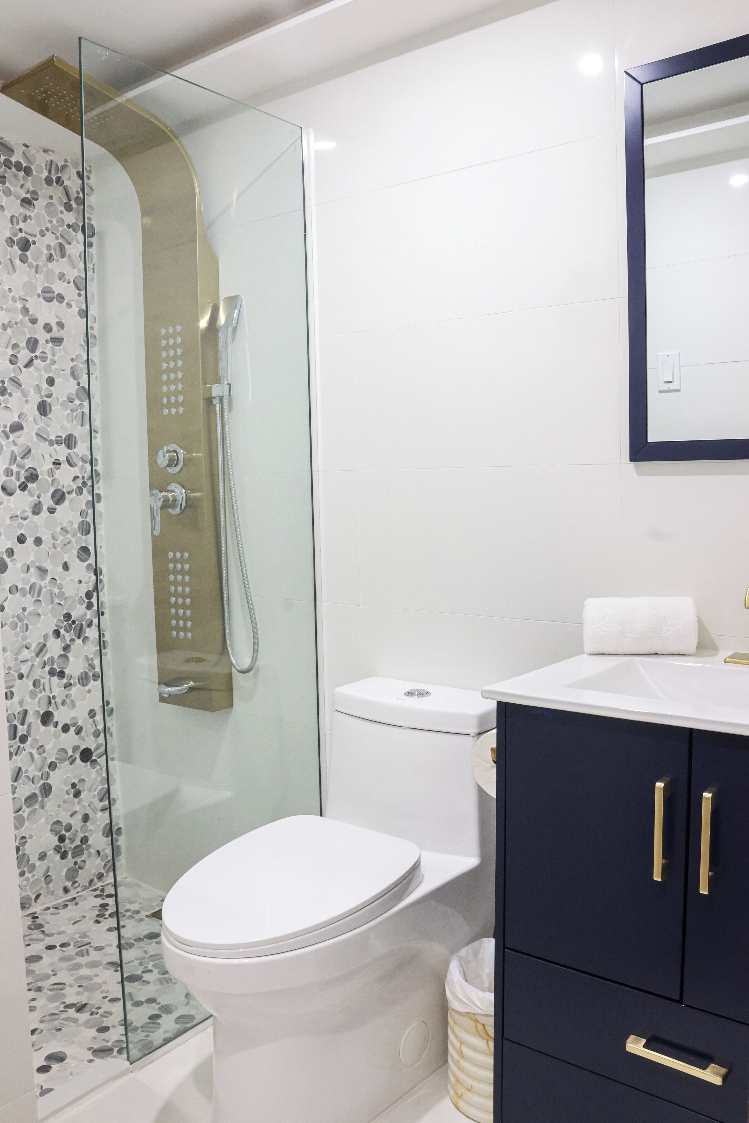 Une salle de bain moderne avec une douche à parois de verre, des toilettes blanches et des meubles bleu foncé dotés de poignées dorées.
